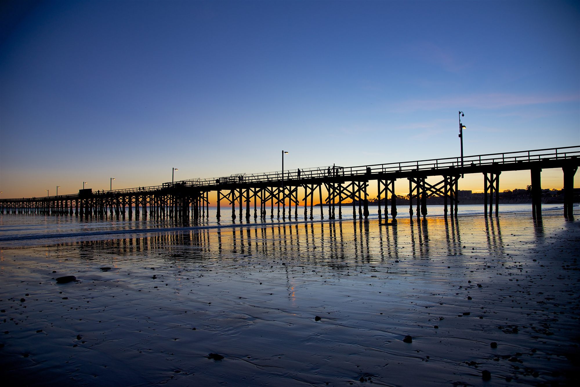 Goleta Pier silhouetted at dusk over the wet sand of Goleta Beach